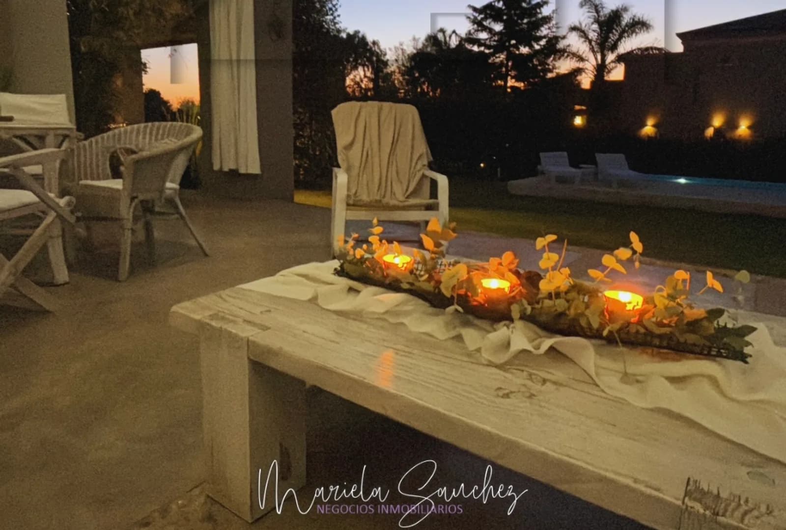 Galería con mesa de madera iluminada con velas al atardecer y la pileta al fondo