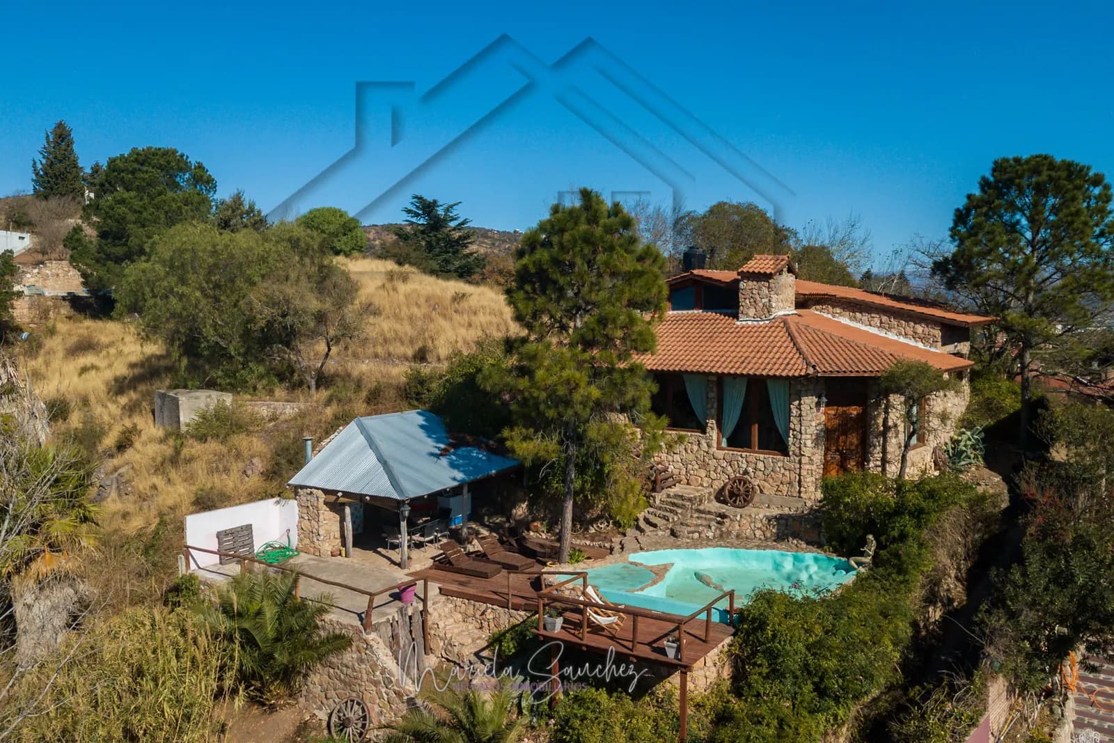 Vista aérea de la casa de piedra con su quincho, la pileta y el deck sobre la ladera